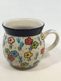 Angled front view of a small 8oz Ceramika Artystyczna Polish pottery bubble mug in the Unikat U4884 pattern, featuring a colorful hand-painted floral design, pastel polka dots, a solid blue rim, and a small portion of the interior.