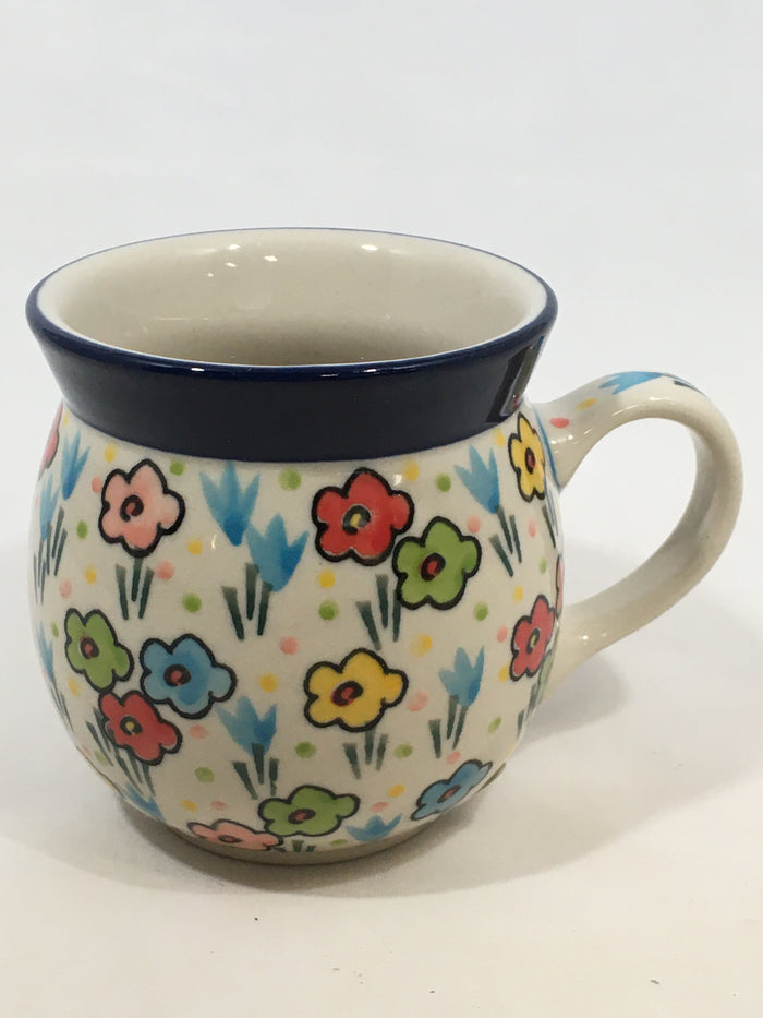 Angled front view of a small 8oz Ceramika Artystyczna Polish pottery bubble mug in the Unikat U4884 pattern, featuring a colorful hand-painted floral design, pastel polka dots, a solid blue rim, and a small portion of the interior.