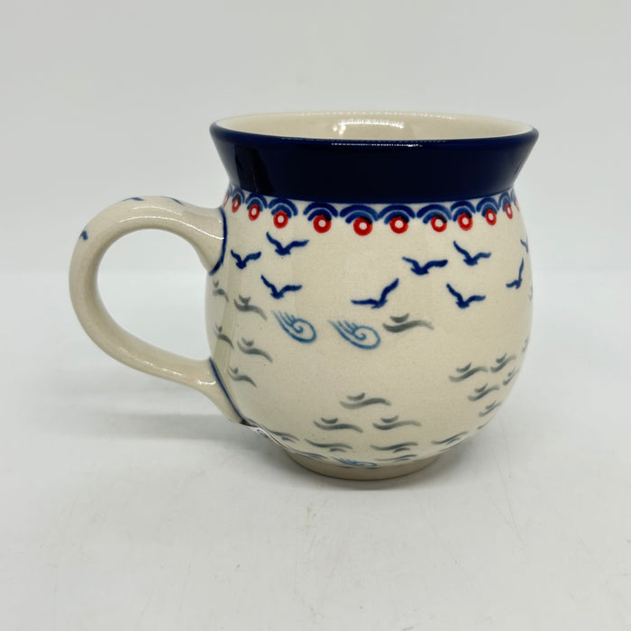 Back view of an 11oz Ceramika Artystyczna Polish pottery bubble mug in the Unikat U5164 pattern, displaying the continuous hand-stamped design of flying blue birds, waves, and a wide blue lip.