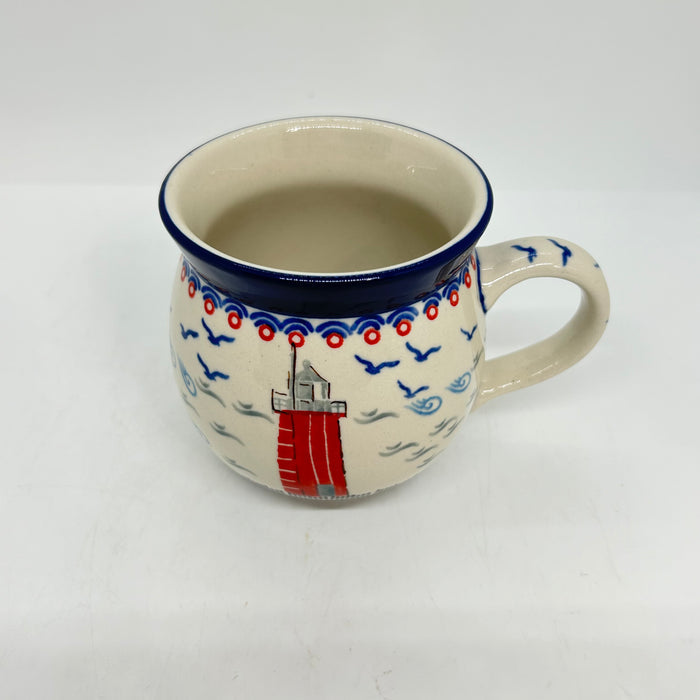 Angled top-down view of an 11oz Ceramika Artystyczna Polish pottery bubble mug in the Unikat U5164 pattern, showing the lighthouse exterior, the wide blue lip, and a clean, undecorated interior.